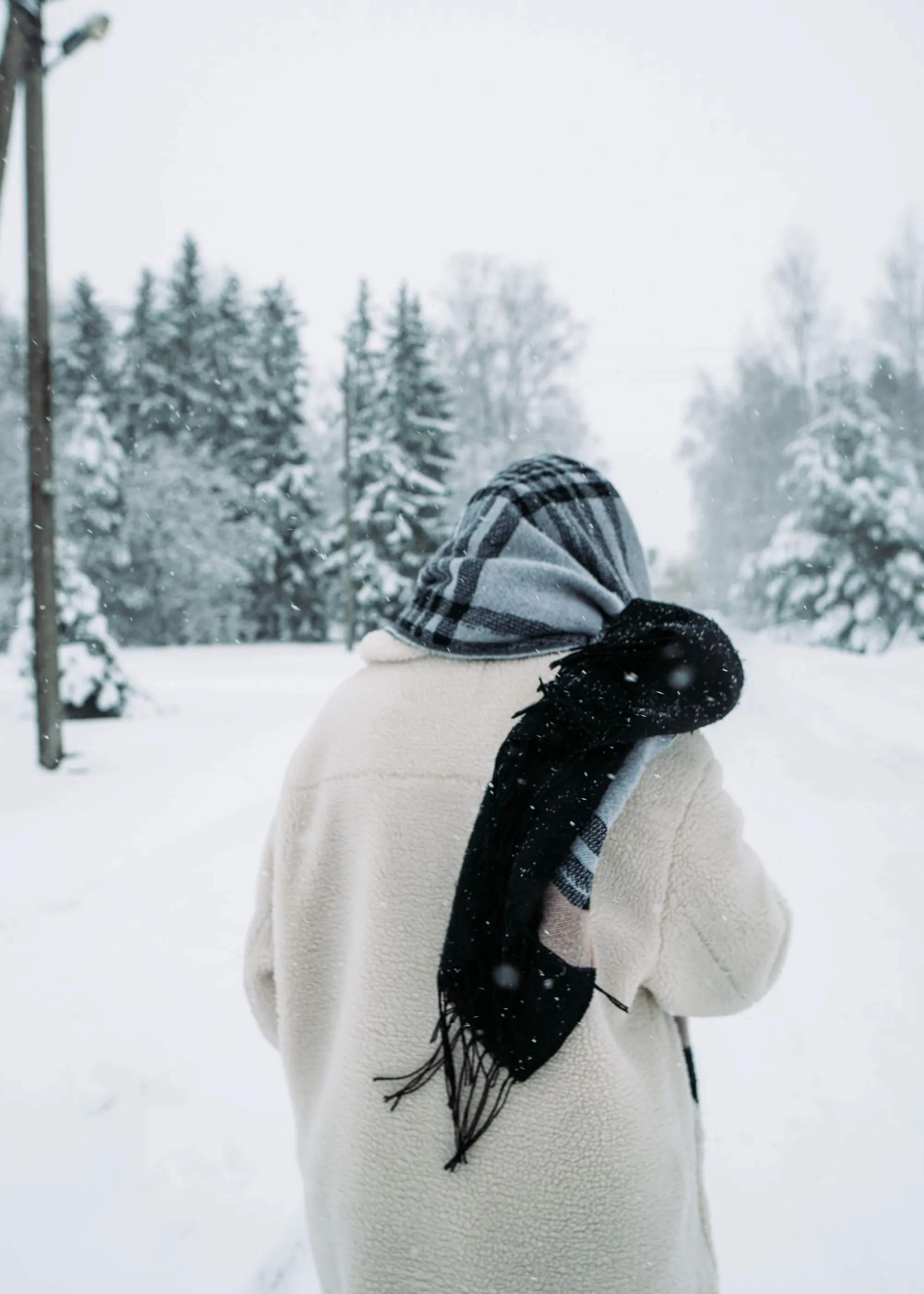 A person in a thick scarf walking through a snowy forest