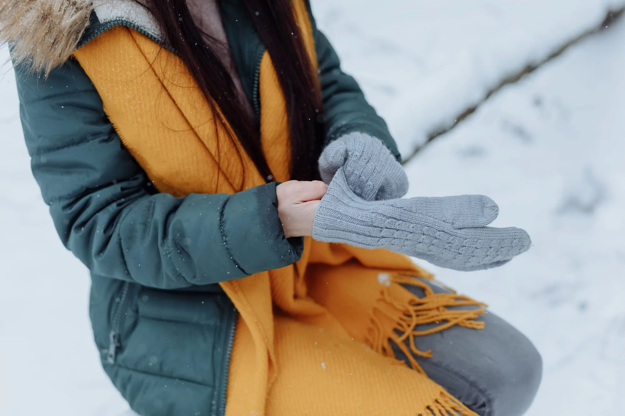 A woman pulling on knit gloves in the snow, standing in for the Tallis Liner Glove