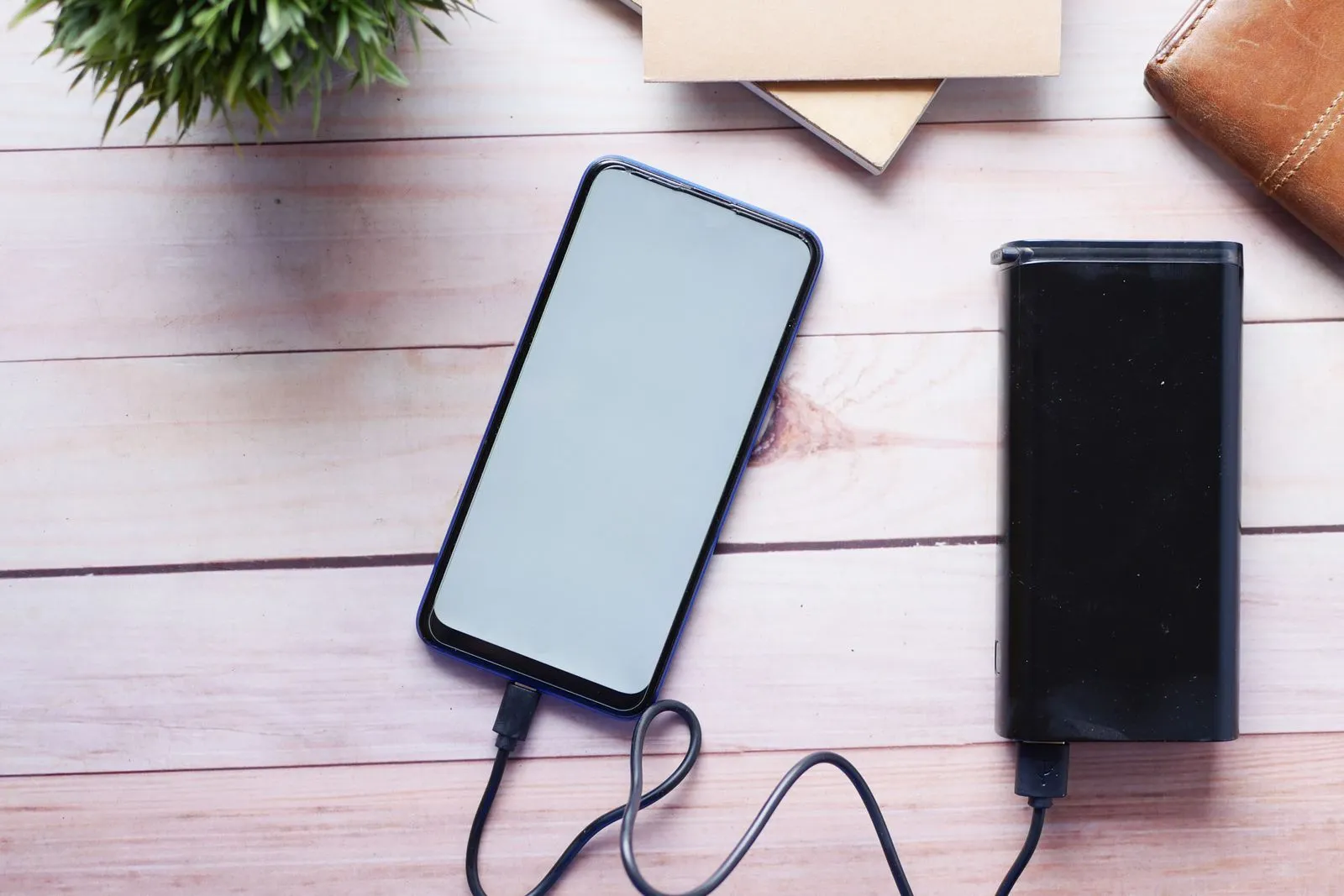 A phone charging from a black battery pack on a wooden table
